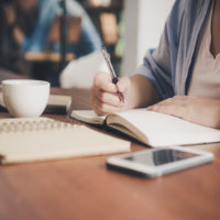 Összesítőt író asszisztens, az asztalon mobil, jegyzetfüzet, egy csésze kávé